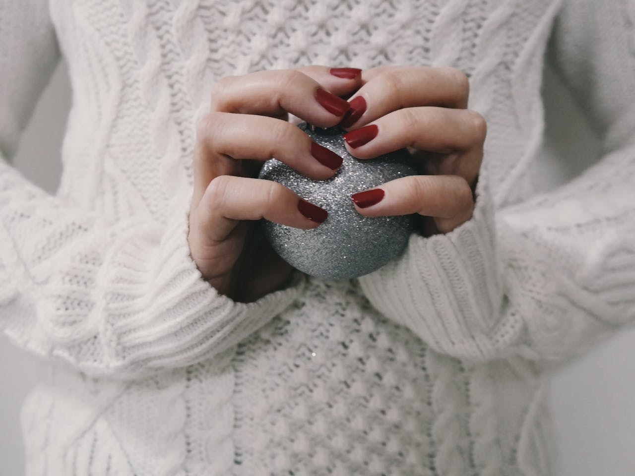 Hands with red manicure holding a silver glitter ball, perfect for winter holiday themes.